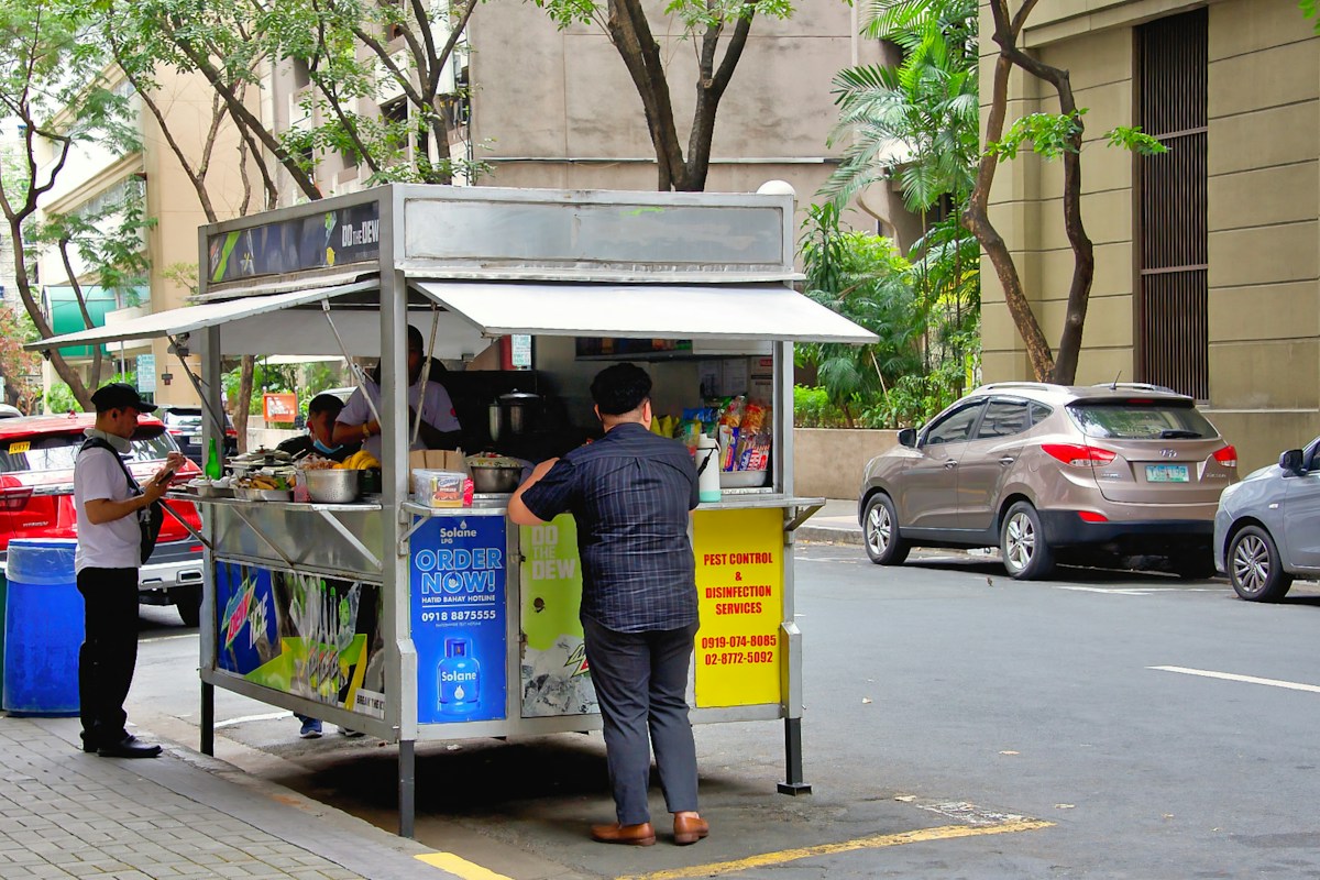 People at a street food cart on a city sidewalk in the Philippines